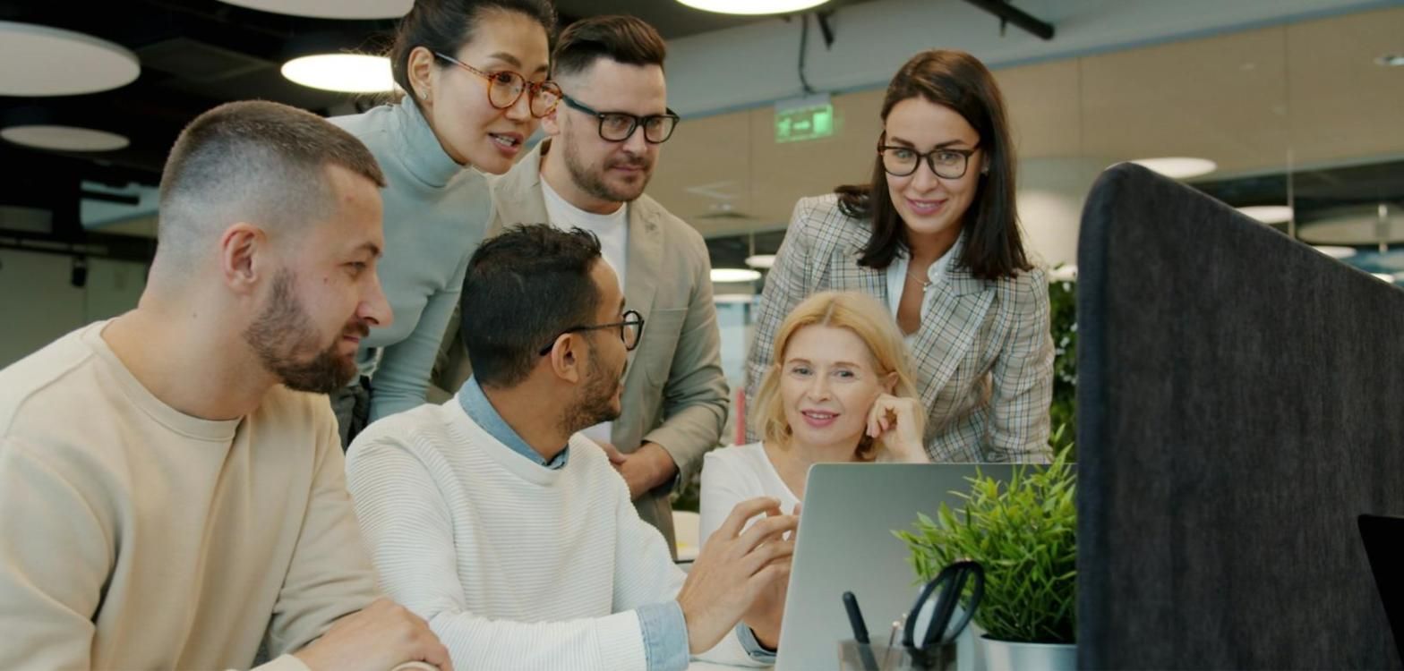 Equipo de oficina reunido alrededor de un portátil revisando datos juntos