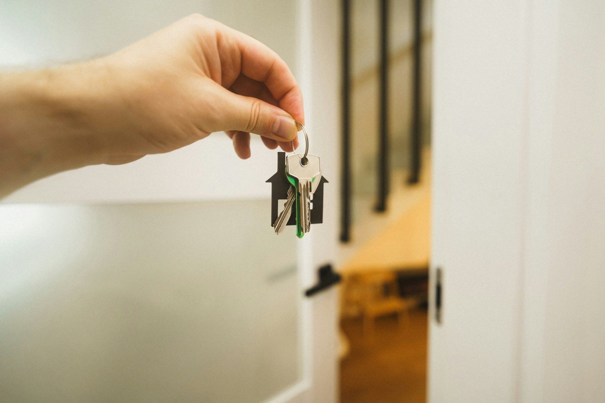 Mano sosteniendo un llavero con forma de casa ante la puerta de una vivienda