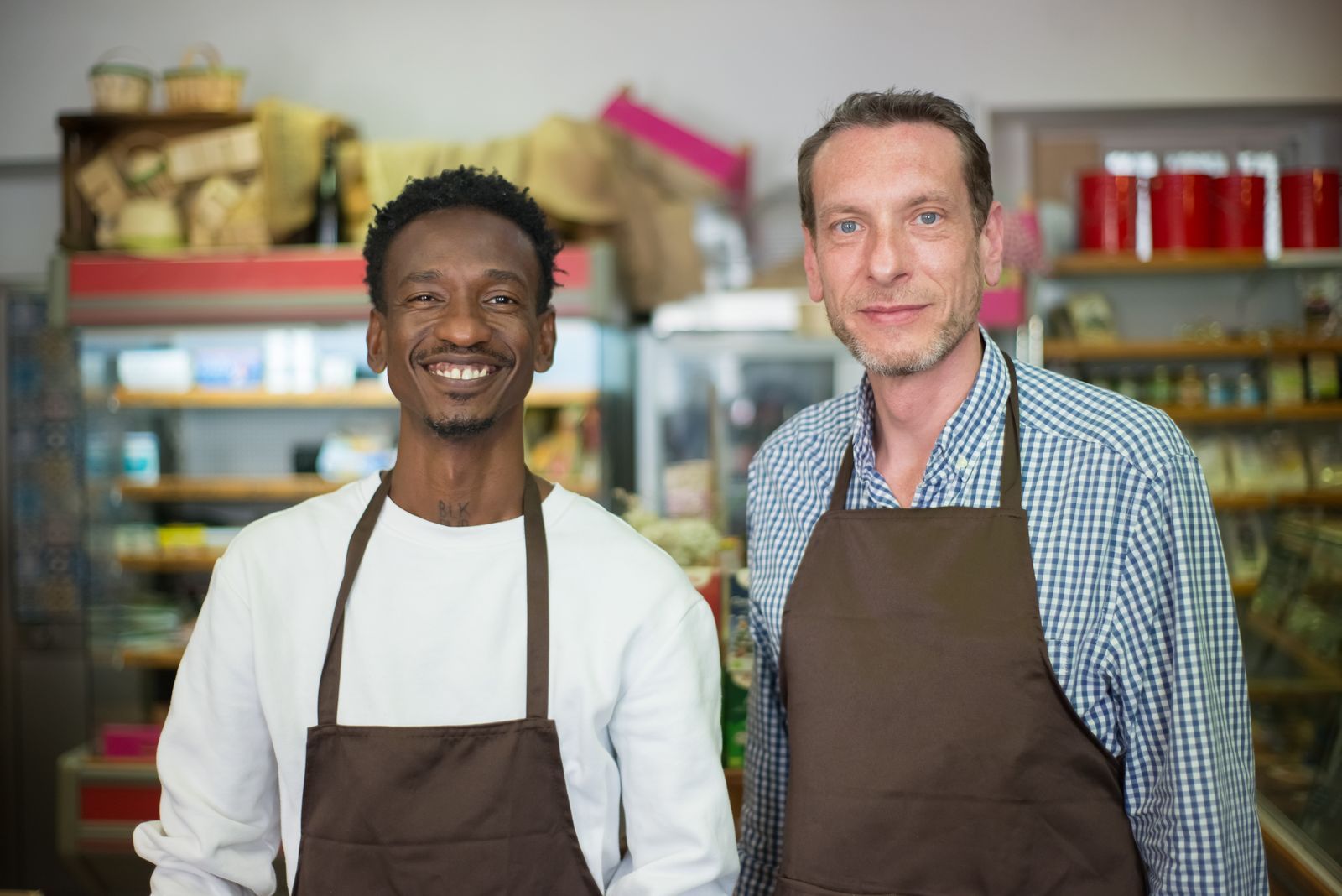Dos comerciantes con delantal sonriendo en su tienda de barrio