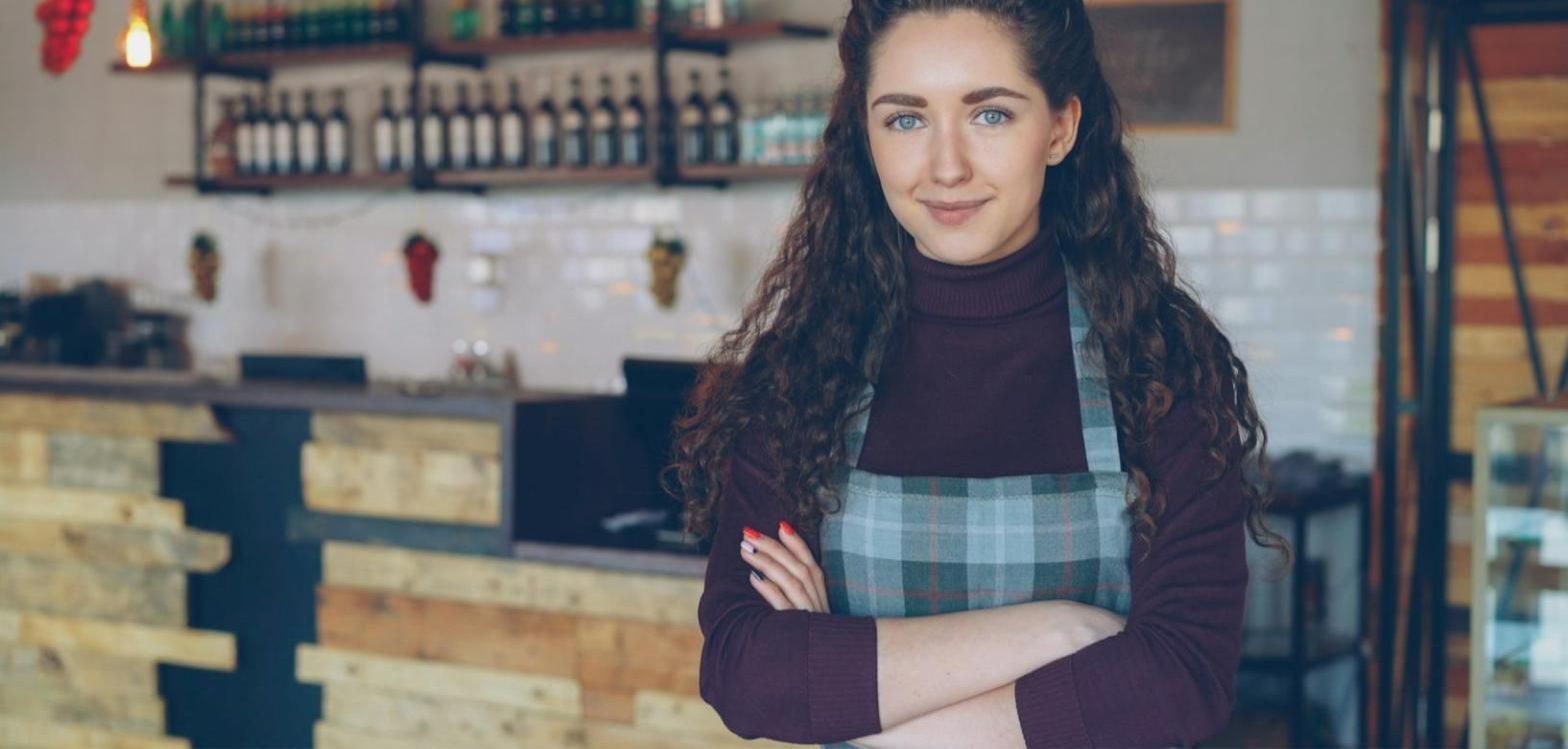 Dueña de una cafetería sonriendo con los brazos cruzados junto al mostrador