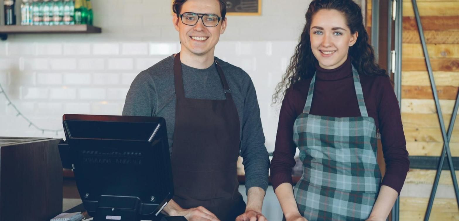 Pareja de hosteleros sonriendo detrás del mostrador con su terminal de venta