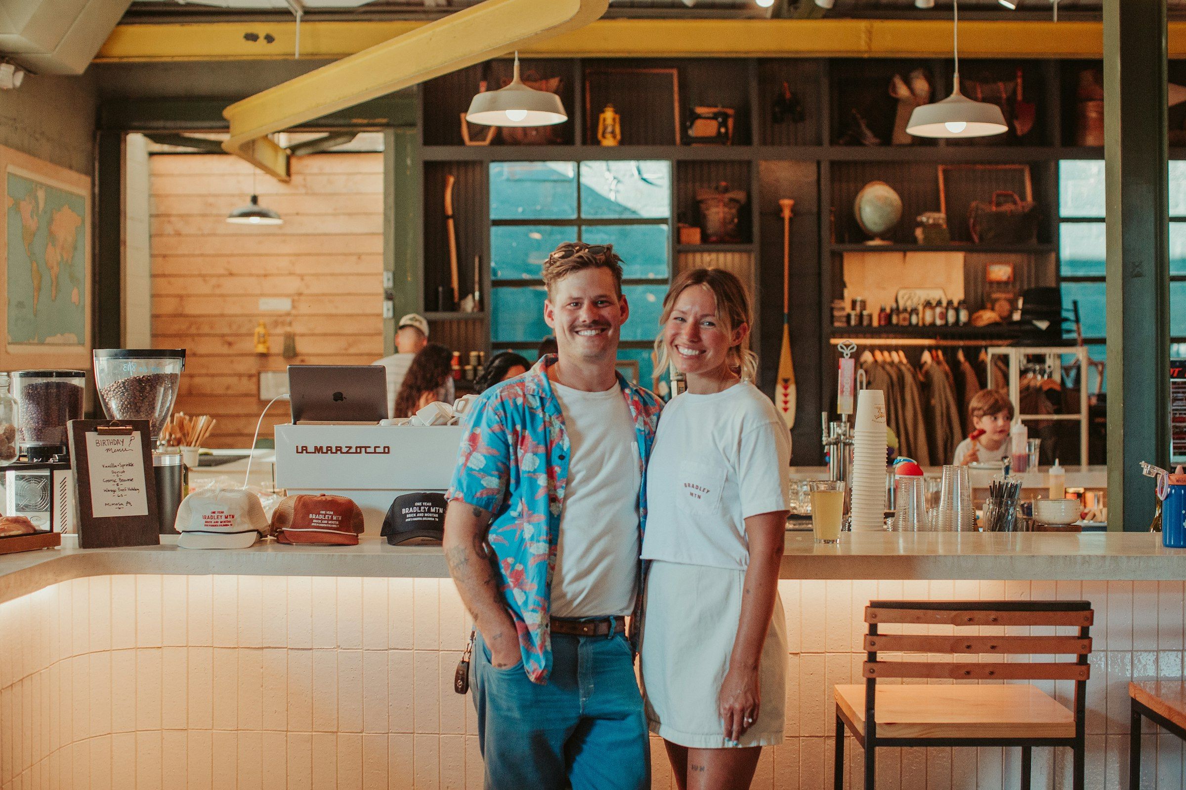 Pareja de dueños de una cafetería sonriendo de pie junto a su barra