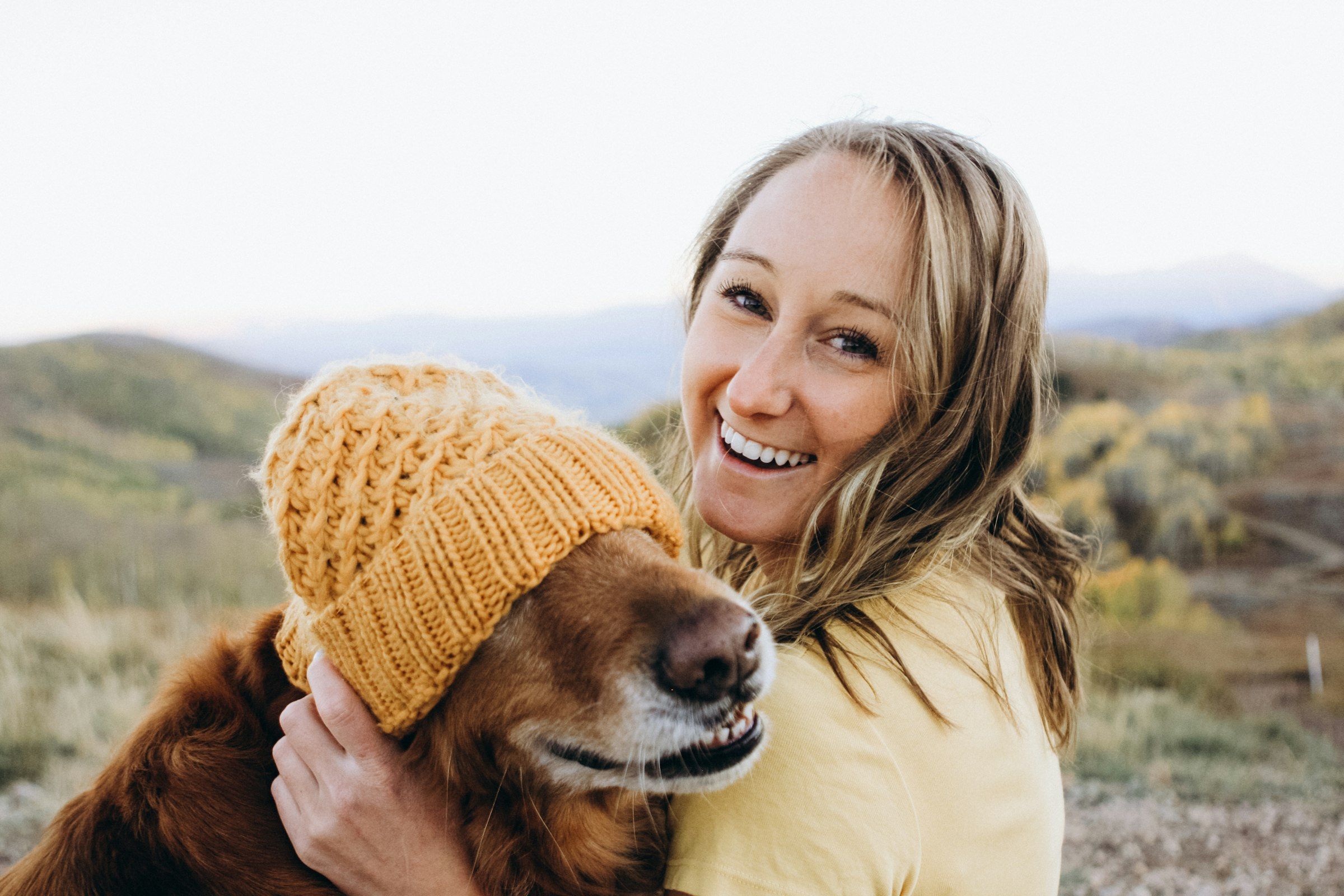 Mujer riendo mientras abraza a su perro, que lleva un gorro de lana